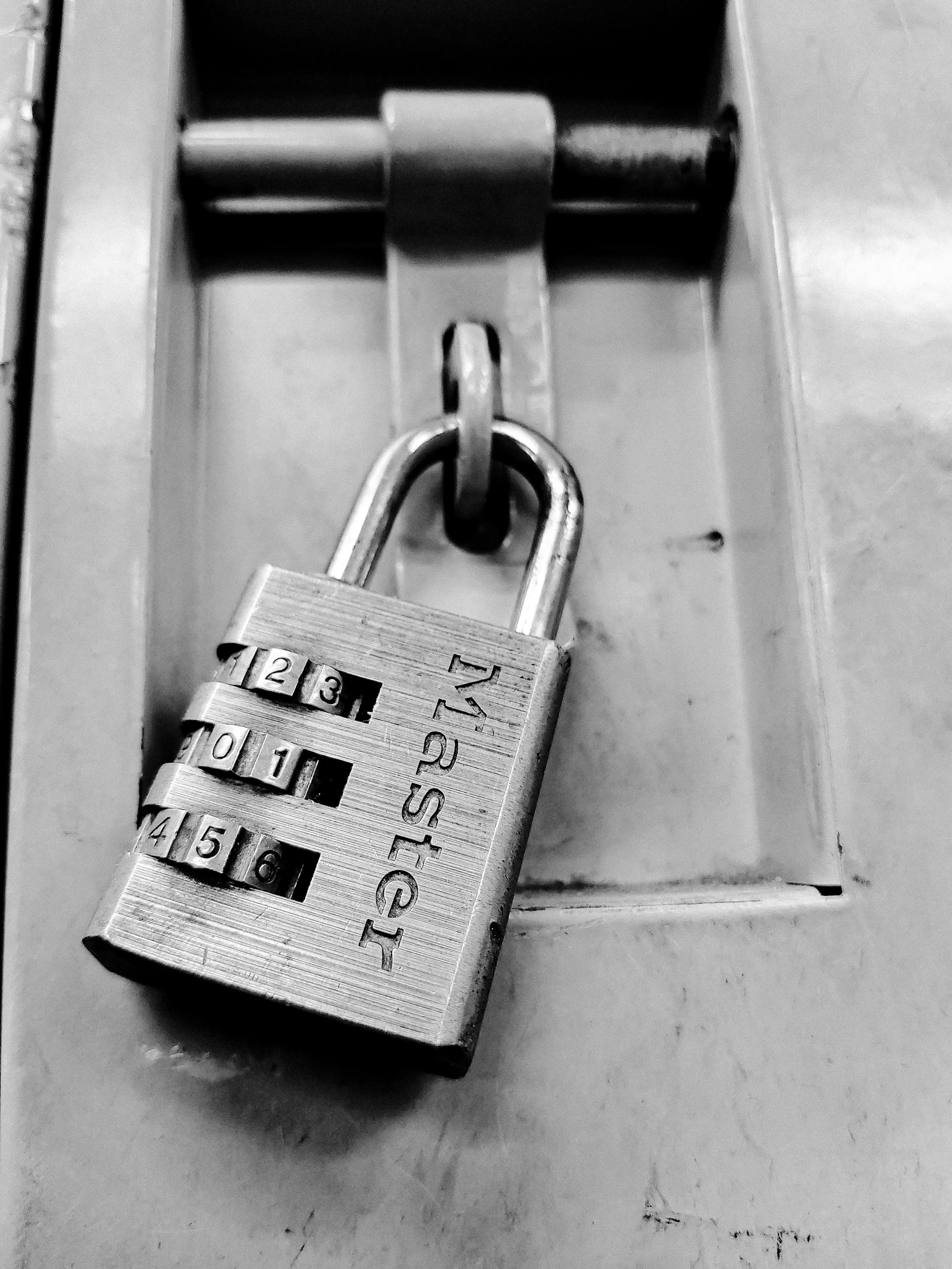 Black and white close-up of a combination padlock on a secure metal locker, symbolizing protection.